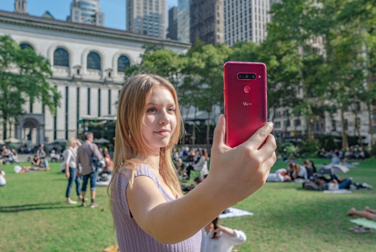 A woman holds up and looks at the display of the LG V40 ThinQ in the Carmine Red color.