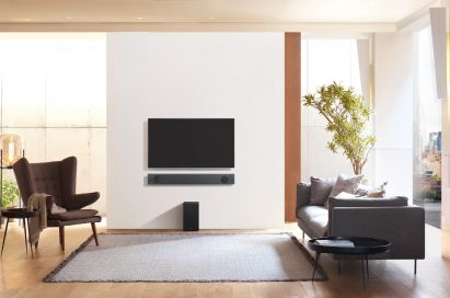 A direct view of the LG Soundbar model SL9YG installed on the wall below an LG TV, with the LG Wireless Rear Speaker Kit model SPK 8 on the floor below