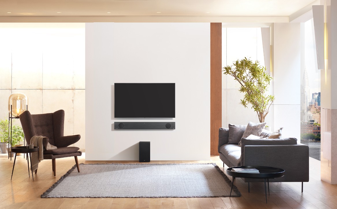 A direct view of the LG Soundbar model SL9YG installed on the wall below an LG TV, with the LG Wireless Rear Speaker Kit model SPK 8 on the floor below