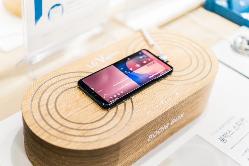 An LG V40 ThinQ is on display at a promotional zone, demonstrating its powerful amplification when placed on a solid surface or box.