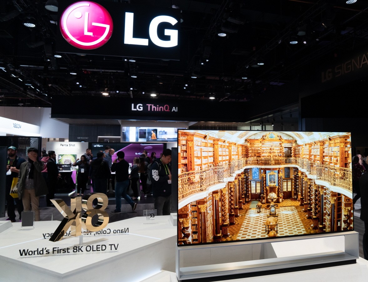 Front view of an LG 8K OLED TV set positioned on the right side of a promotional sign saying "World's First 8K OLED TV"