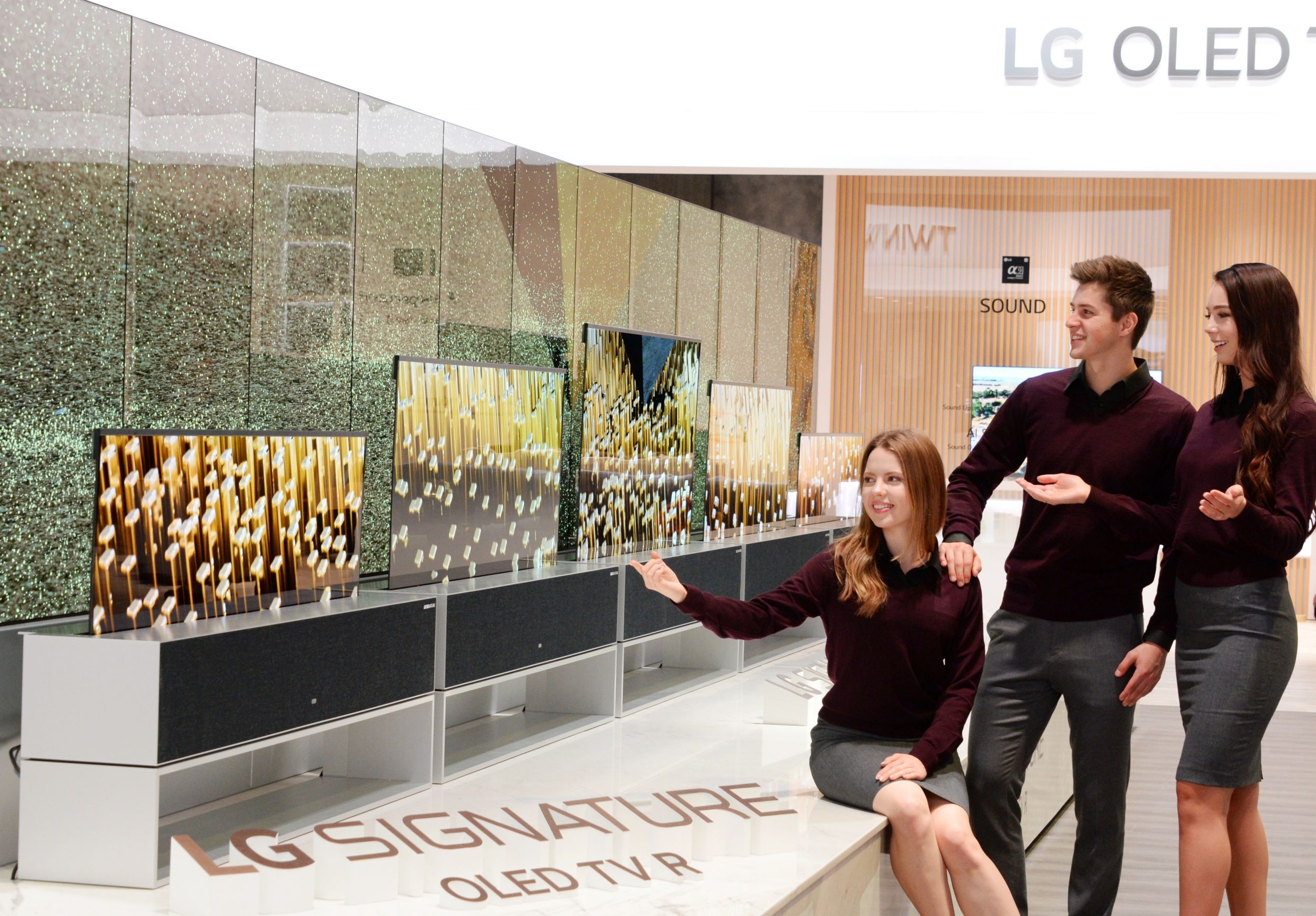 Three people are looking at LG OLED TV R on display at LG’s CES 2019 booth