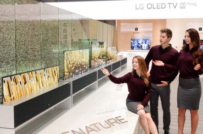 Three people are looking at LG OLED TV R on display at LG’s CES 2019 booth