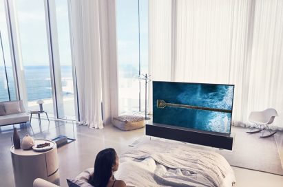A woman enjoying watching her LG OLED TV R in its Full View mode positioned at the end of her bed
