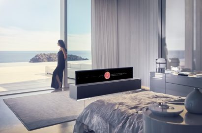 A view of the LG OLED TV R’s Line view while positioned at the end of a bed, with a woman leaning against a large window in the background