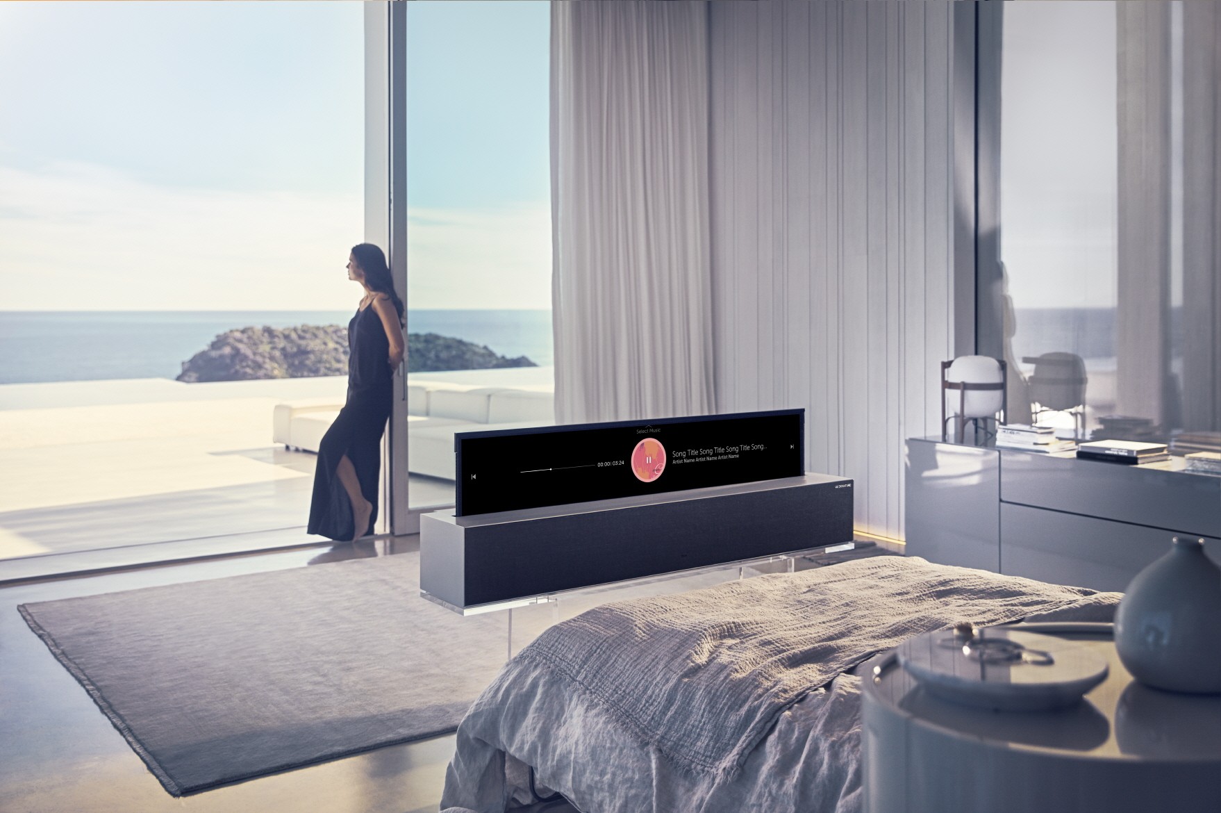 A view of the LG OLED TV R’s Line view while positioned at the end of a bed, with a woman leaning against a large window in the background