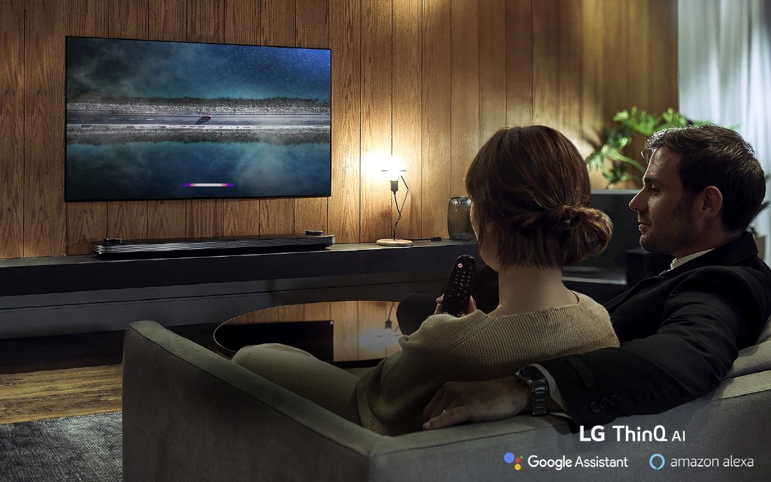 A couple using the LG ThinQ AI TV while sitting on their living room sofa