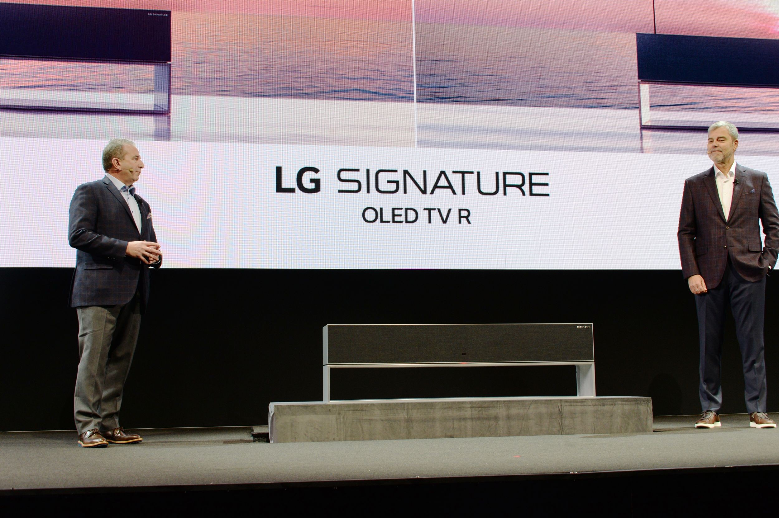 David VanderWall, Senior Vice President of Marketing at LG Electronics USA and Tim Alessi Senior Director of Product Marketing for Home Entertainment Products at LG Electronics USA are onstage discussing the LG SIGNATURE OLED TV R at LG's CES 2019 Press Conference while putting the TV between them.