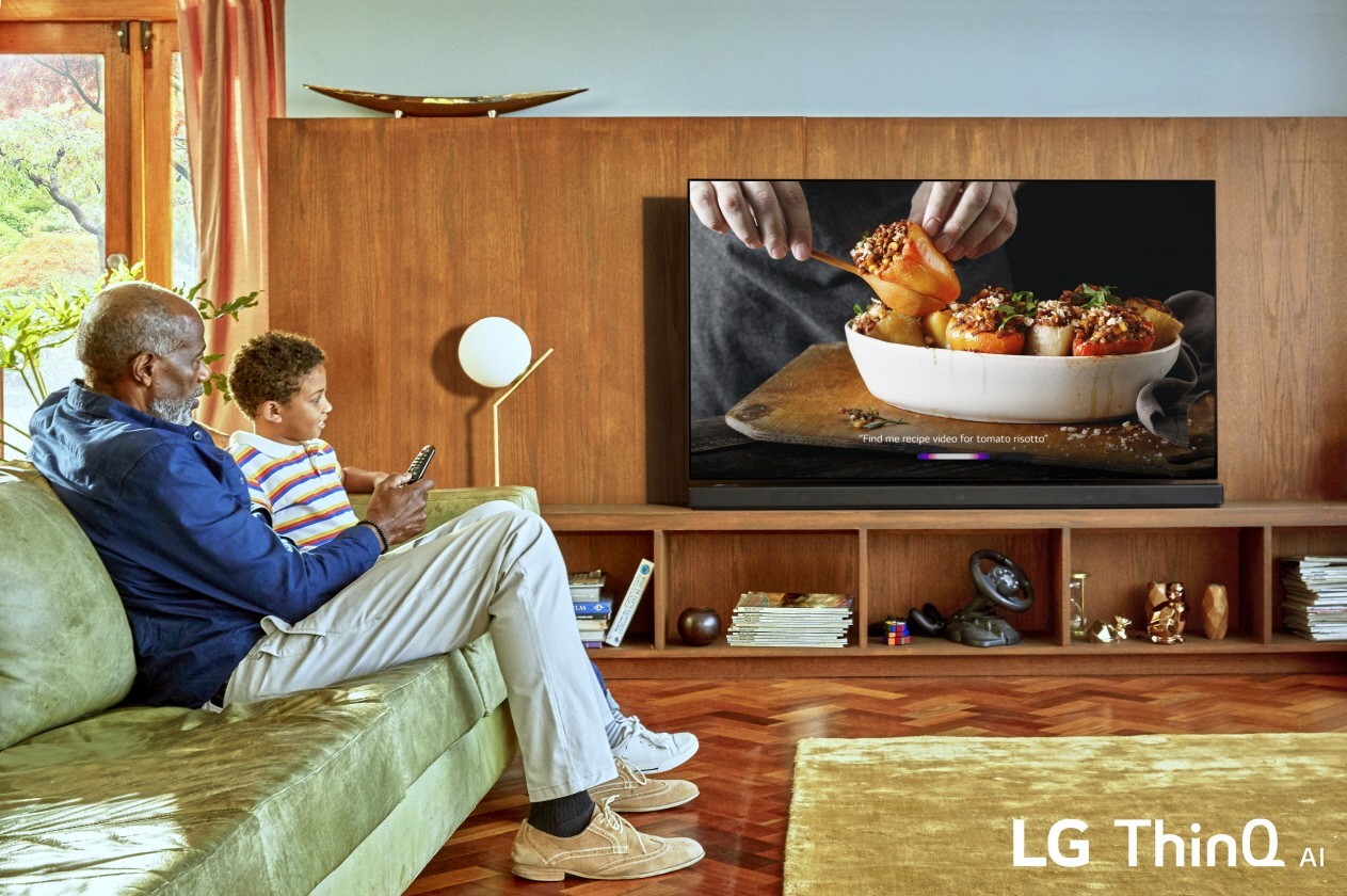 A grandfather watches the LG ThinQ AI TV at home with his grandson