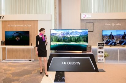 A female model posing in front of LG OLED TV with other LG TV products in behind.