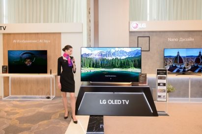 A female model posing in front of LG OLED TV with other LG TV products in behind.