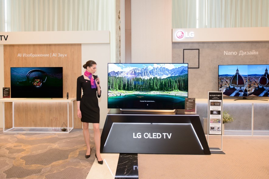 A female model posing in front of LG OLED TV with other LG TV products in behind.