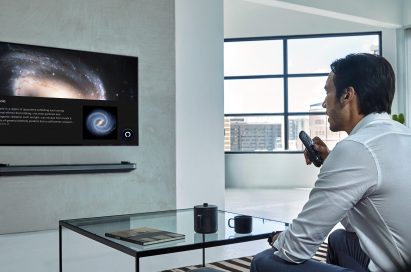 A man is watching LG TV supporting Amazon Alexa while holding the remote in one hand at home
