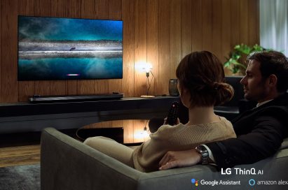 A couple is watching an LG TV supporting Amazon Alexa while the woman holds the remote in one hand