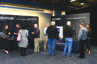 Attendees talk to each other in front of the promotion booths of LG’s technology and service partners, Barco and Chief.