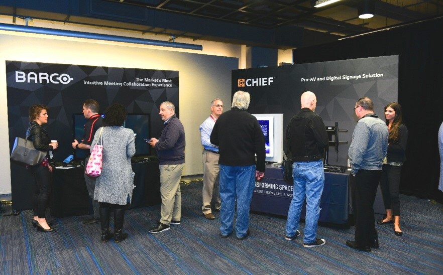 Attendees talk to each other in front of the promotion booths of LG’s technology and service partners, Barco and Chief.
