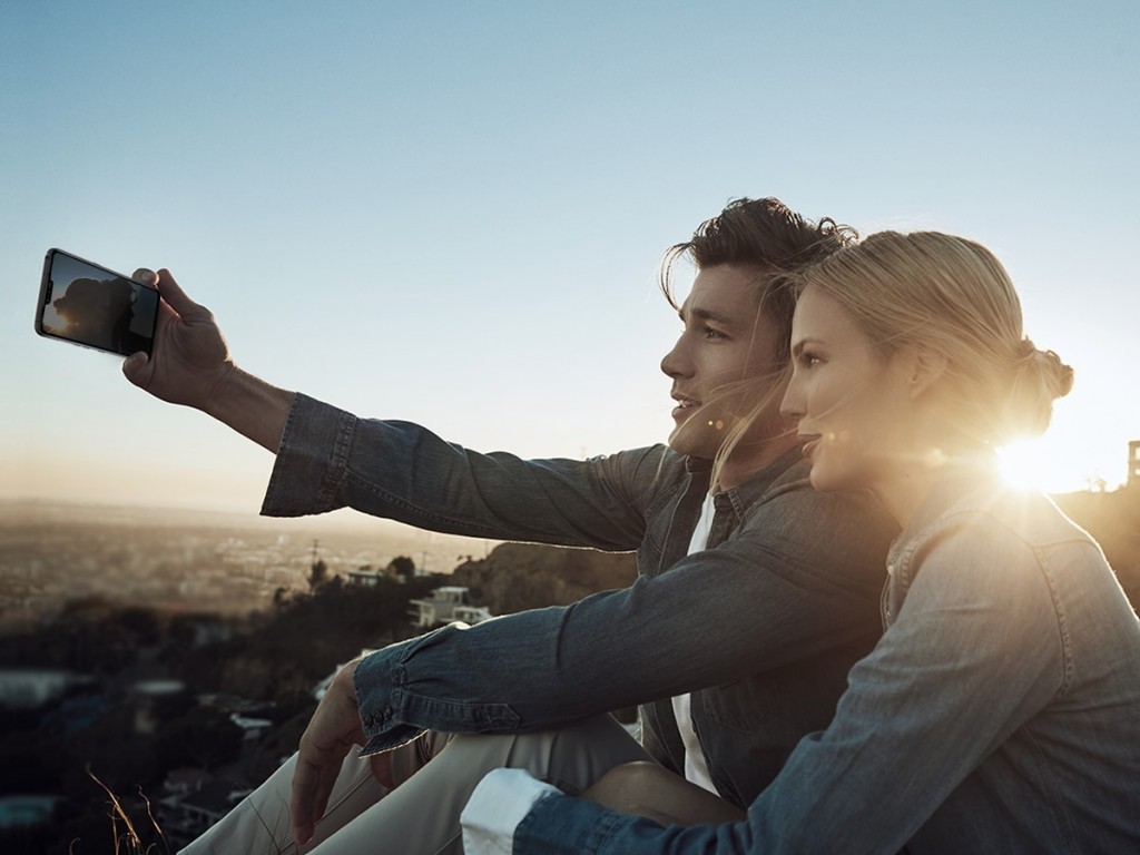 A man holds the LG V50 ThinQ out to take a selfie with a woman with the sunset in the background.
