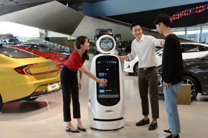 Three visitors interact with LG CLOi GuideBot in front of vehicles at Hyundai Motor Studio Goyang.