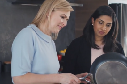 Two ladies behold ingredients while pouring them down from a pen.