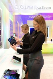 Two female models look at LG G8X ThinQ with the Dual Screen feature in front of some samples of the LG G8X ThinQ phones.
