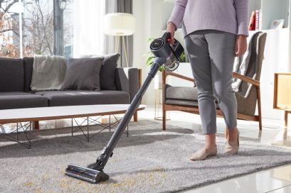 A woman vacuuming her living room carpet with LG CordZeroThinQ A9 Stick Vacuum, which is absorbing dust from the carpet.