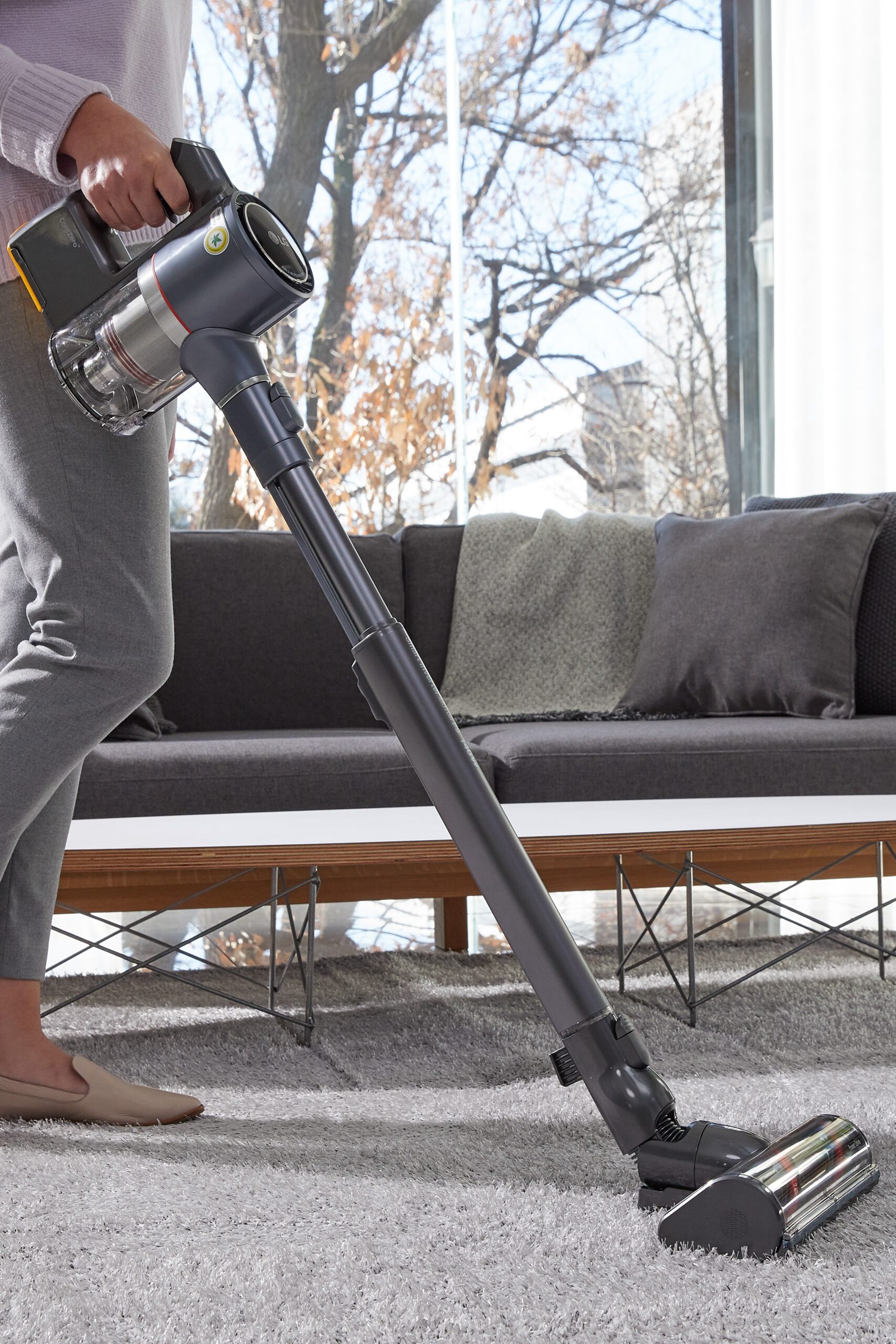 A closer look at LG CordZeroThinQ A9 Stick Vacuum as a woman uses it to clean her living room carpet.