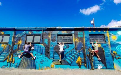 A photo taken by LG G8X ThinQ of three children scaling the side of a building decorated with colorful blue and yellow graffiti.