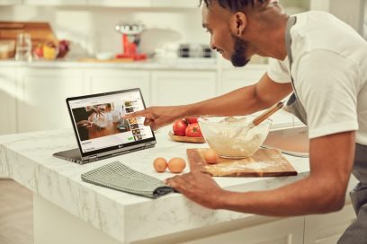 A man pointing at his LG gram model 14T90N’s display while following a cooking demonstration video as he prepares his food