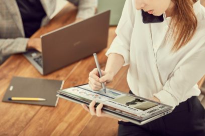 A close-up of a woman holding up her LG gram model 14T90N in one hand, and making notes on it via the handy Stylus Pen with the other