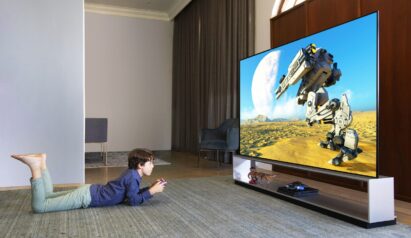 A boy enjoying the big-screen gaming experience on LG 8K OLED TV model ZX as he lays on a cozy living room floor