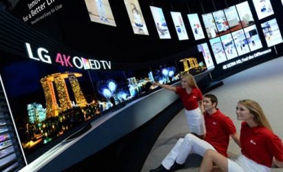 Three models sit down on the floor and look up to the world's first LG 4K curved OLED TV products that are positioned on a display stand.