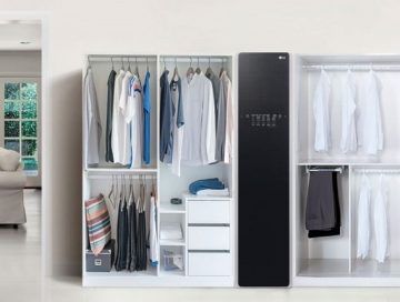 The LG Styler is placed in a room between two white open wardrobes full of clothes