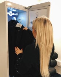 A woman puts her black smart coat inside the LG Styler at the event