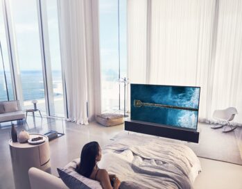 A woman in bed watching an LG SIGNATURE OLED TV R at a bright, beachside mansion.