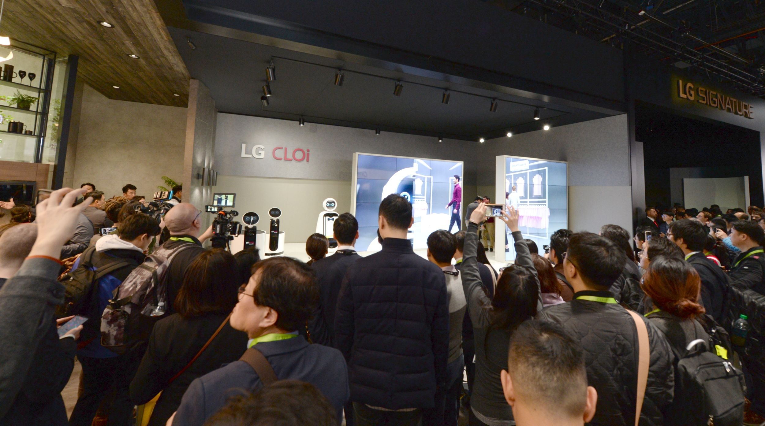 Far shot of a demonstration session for LG's CLOi commercial robots with attendees watching a presentation at the company's CES 2019 booth