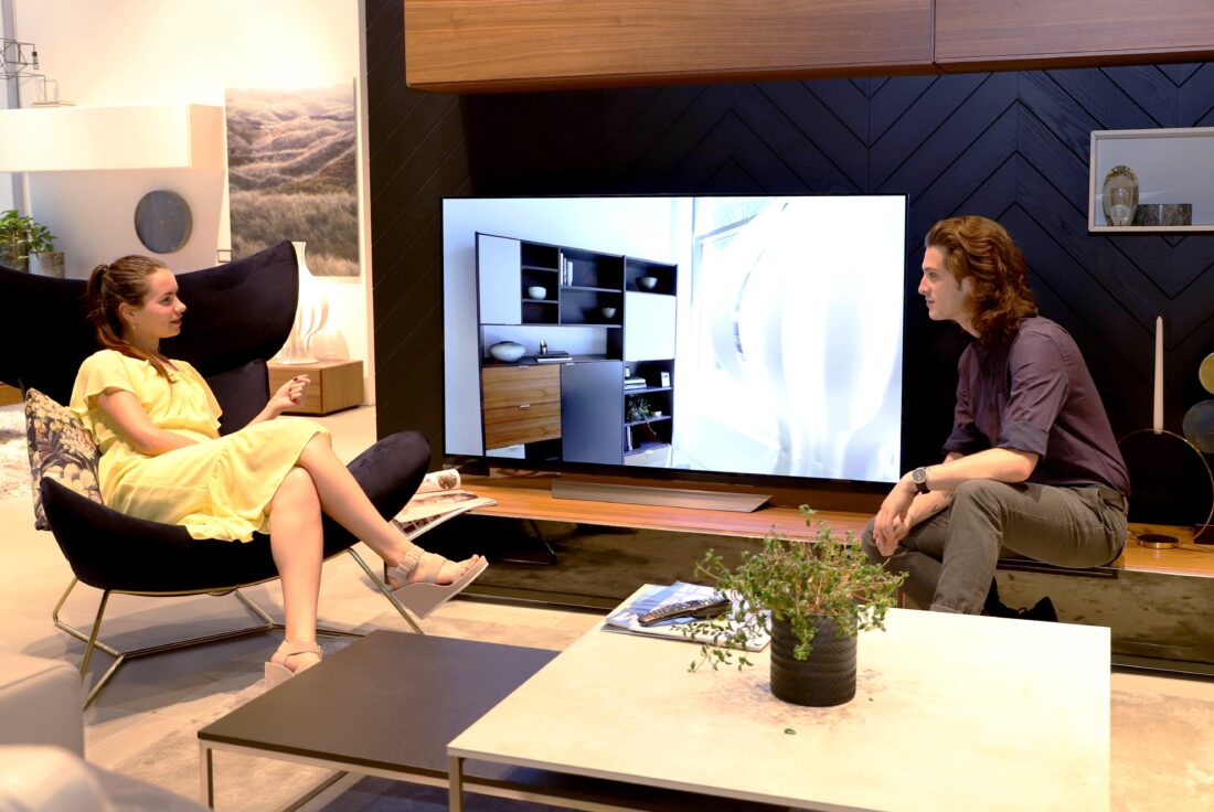 A man and a woman sit in the sample AI-enabled living room discussing LG's AI ThinQ-enabled TVs