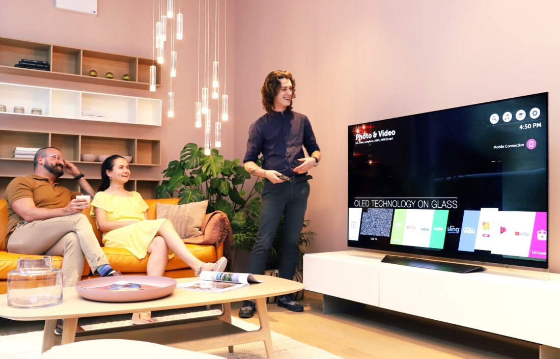 A male attendant tries out the AI assistant features of LG’s ThinQ-eabled OLED TV which displays the application bar of webOS platform on the screen