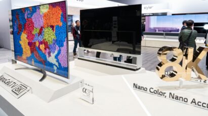 Two LG 8K NanoCell LCD TV models that are positioned the front and the back next to a rotating 8K promotional sign board