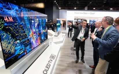 Side view of the display zone of LG's 8K OLED TV, the TV is to the left and a group of attendees on the right admire its excellent features.