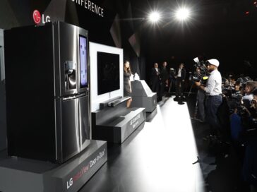 Side view of a female model posing next to LG SIGNATURE OLED TV W and LG CLOi Robots on stage while reporters take pictures at LG's CES 2017 Press Conference.