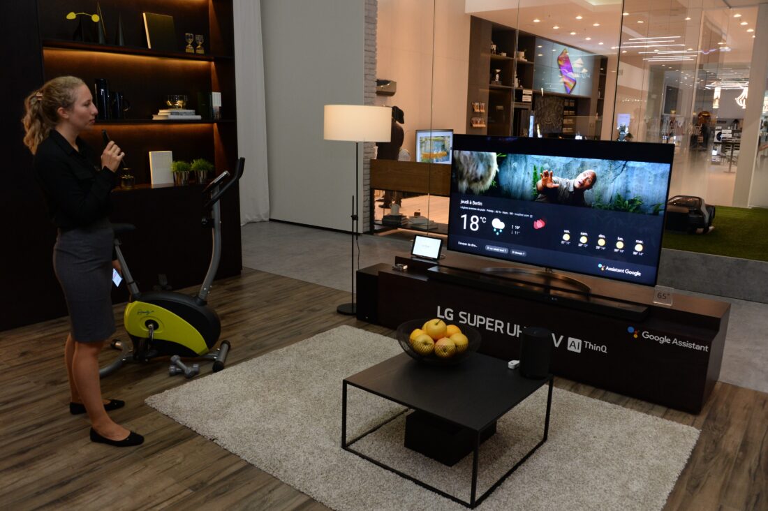 A female attendant holding the Magic Remote stands next to the LG SUPER UHD TV AI ThinQ with Google Assistant to try out the AI voice assistant feature.