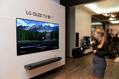 View of LG OLED TV AI ThinQ display zone, a female attendant tries out the TV's AI voice assistant features with the Magic Remote