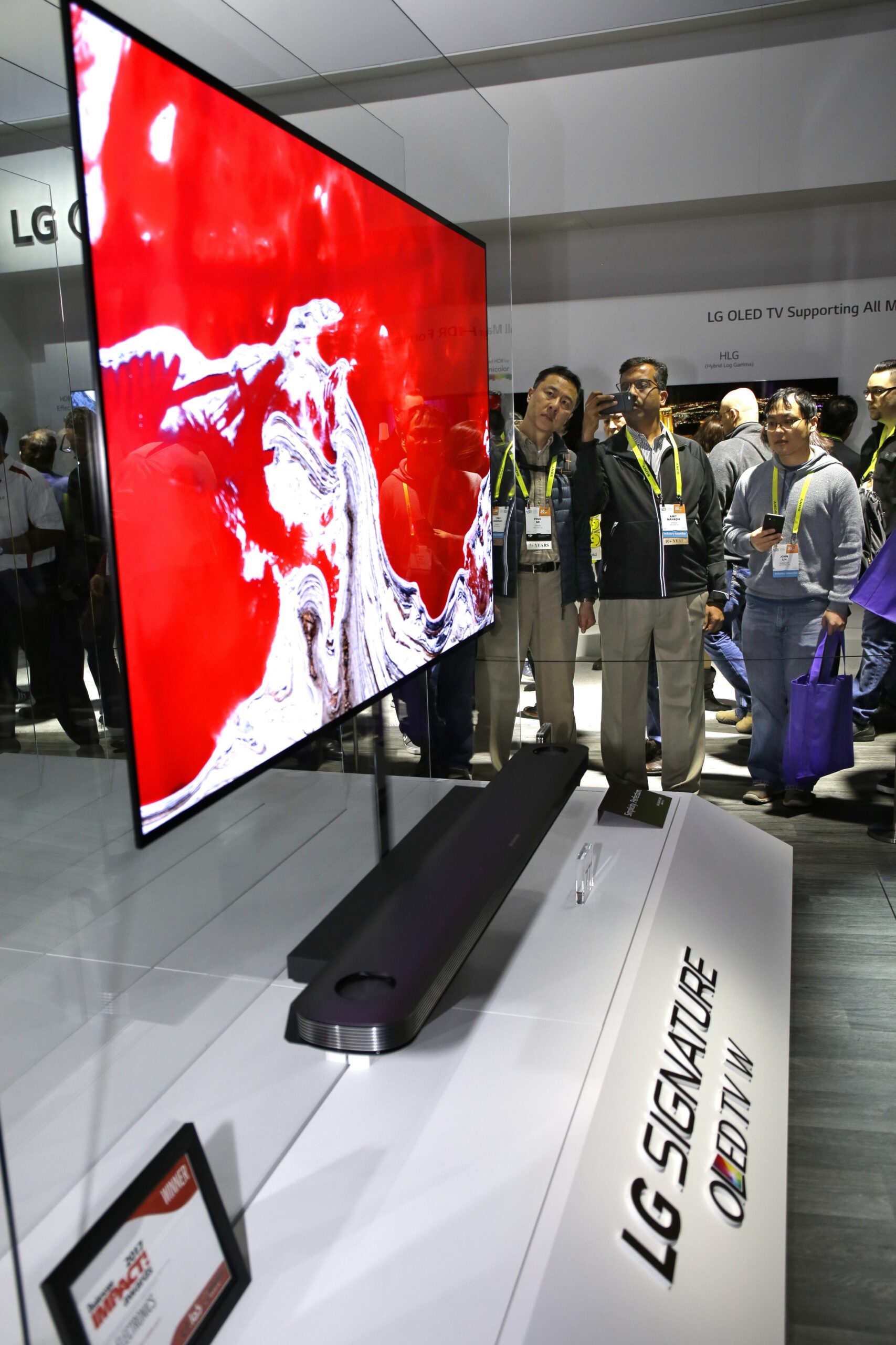 Side view of LG SIGNATURE OLED TV W display with conference attendees examining its incredibly thin display at the model at CES 2017