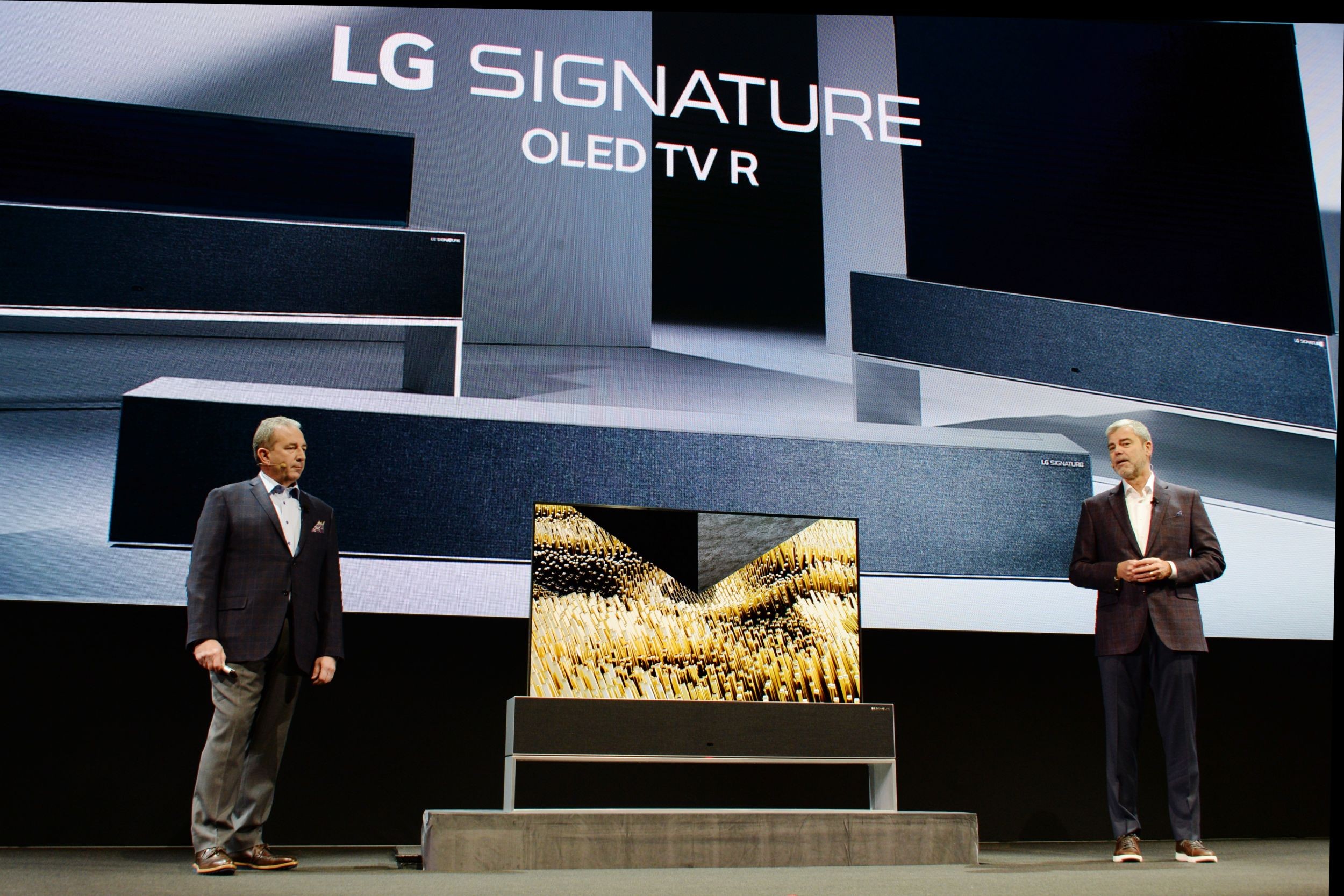 David VanderWall, Senior Vice President of Marketing at LG Electronics USA and Tim Alessi Senior Director of Product Marketing for Home Entertainment Products at LG Electronics USA are onstage discussing the LG SIGNATURE OLED TV R at LG's CES 2019 Press Conference while putting the TV between them.