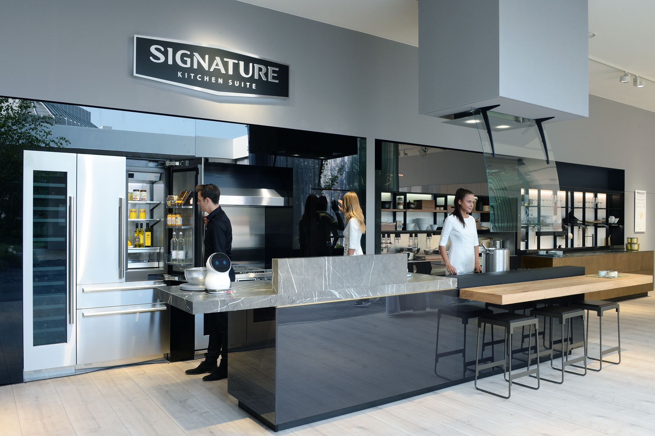 Another view of the LG Signature Kitchen Suite display zone, three models are standing in the kitchen.