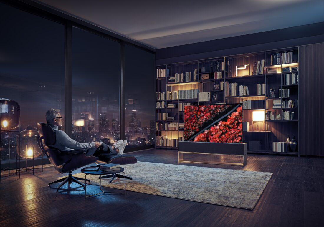 A man is relaxing in a chair at night, watching a nature scene on an LG SIGNATURE OLED TV R