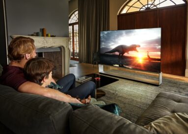 Father and son sit together in their living room to watch dinosaurs come to life on their LG TV