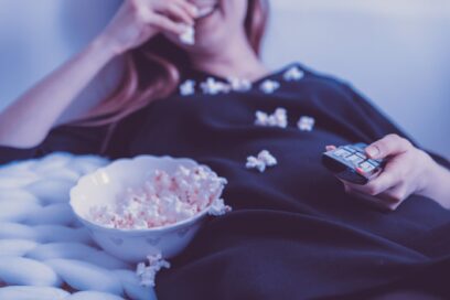 A woman holding the TV remote while eating popcorn