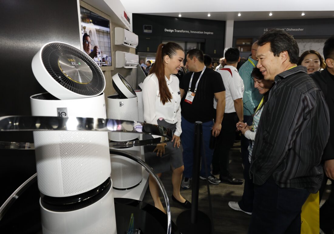 A female attendant stands next to the LG PuriCare Air Purifier talking to conference attendees in the LG display zone at CES 2017.