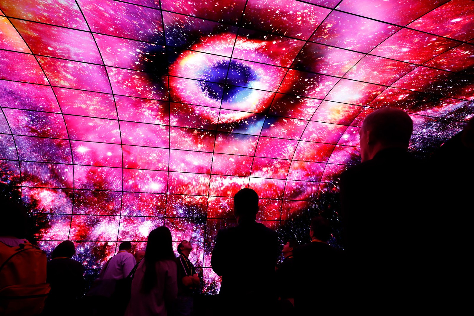 Visitors stand underneath LG OLED Tunnel and look up the screens.